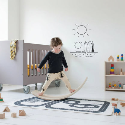 Child standing on a balance board in a room with a crib and toys.